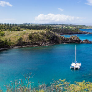 A lone sailboat sitting in a bright blue lagoon along a green forest in Maui. Original public domain image from Wikimedia Commons